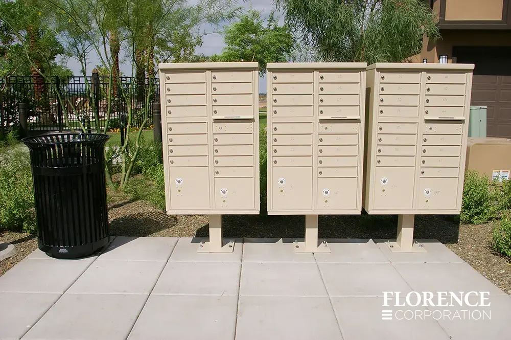 vital&trade; cluster box units in sandstone installed near recreation center of townhome community near black waste bin surrounded by greenery and landscaping