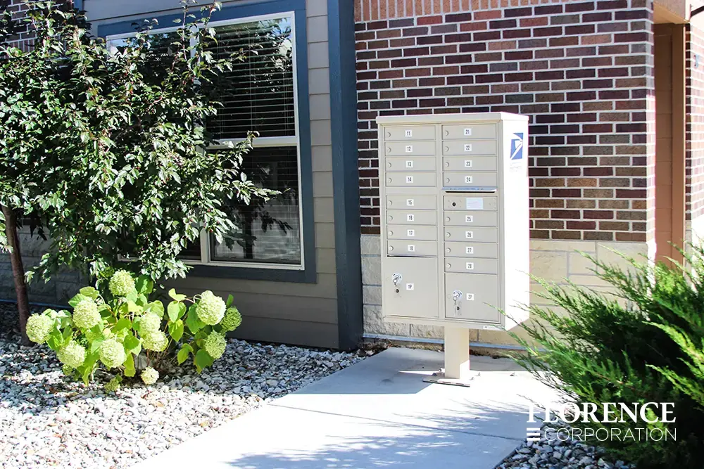 Single vital&trade; cluster box unit in sandstone installed outside of red brick apartment building near shrubbery and hydrangea garden.