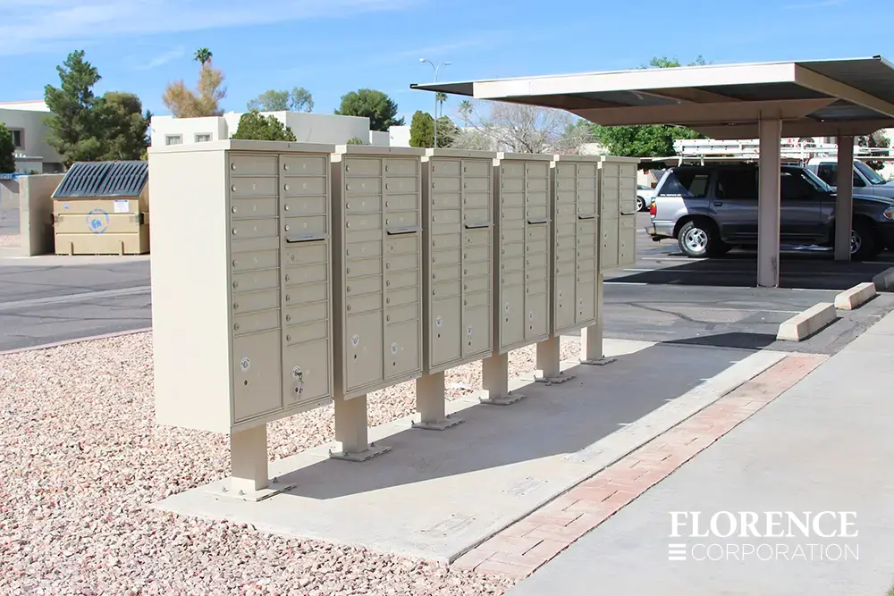 vital&trade; cluster box units in sandstone installed in a parking lot near covered awning with rock landscaping