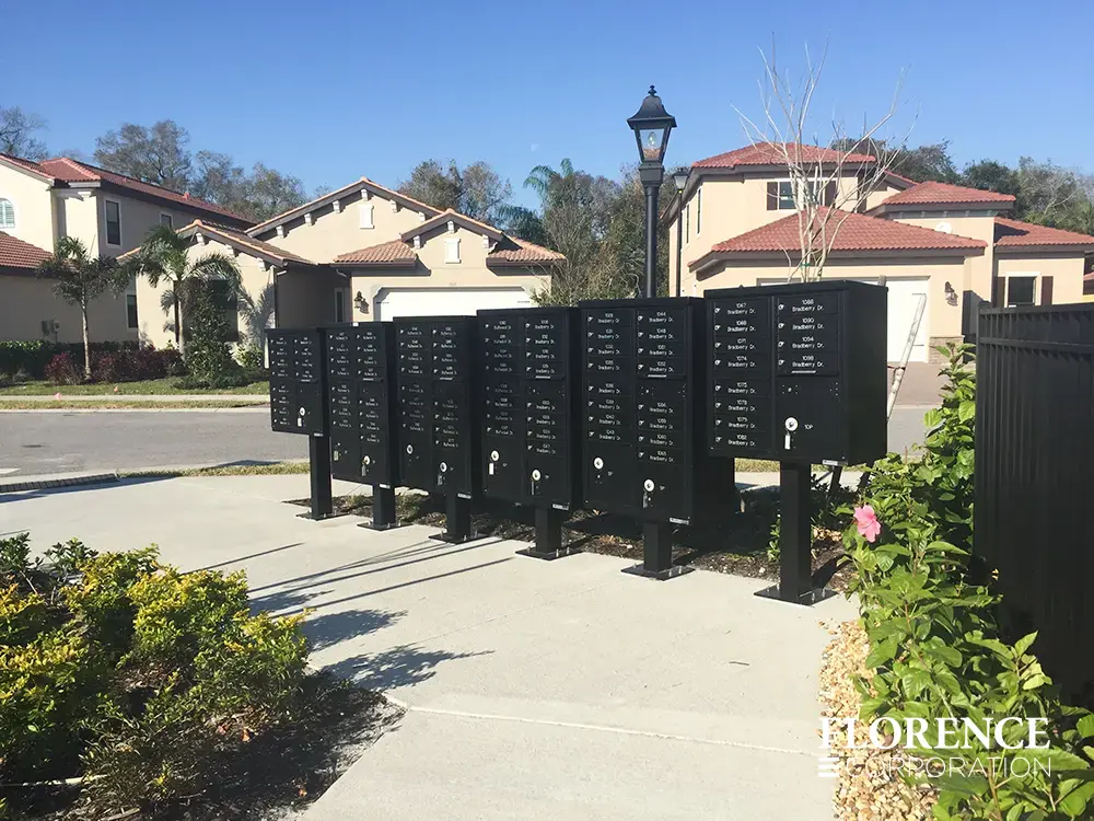 vital&trade; cluster box units in black with custom engraving addresses installed near hibiscus flower bush in single family home development