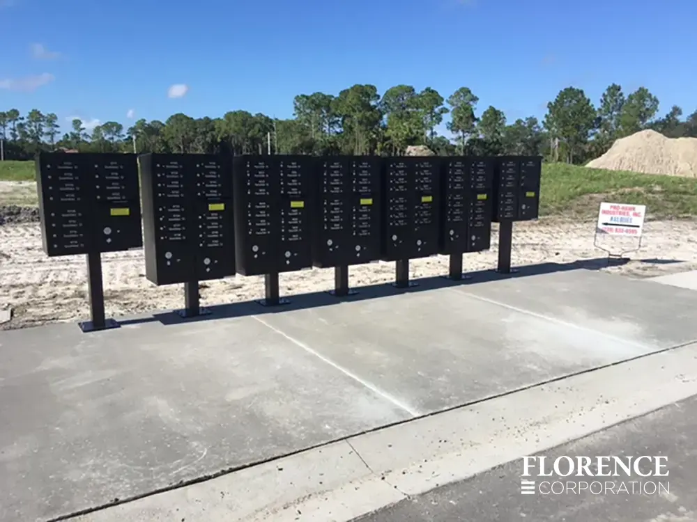 vital&trade; cluster box units in black installed on large concrete slab near new construction site with a bright blue sky and green trees in the background