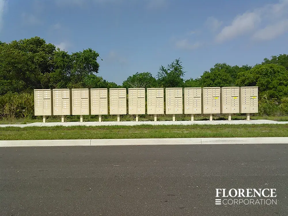 vital&trade; cluster box units in sandstone installed in long row along road with a blue sky and trees in the background