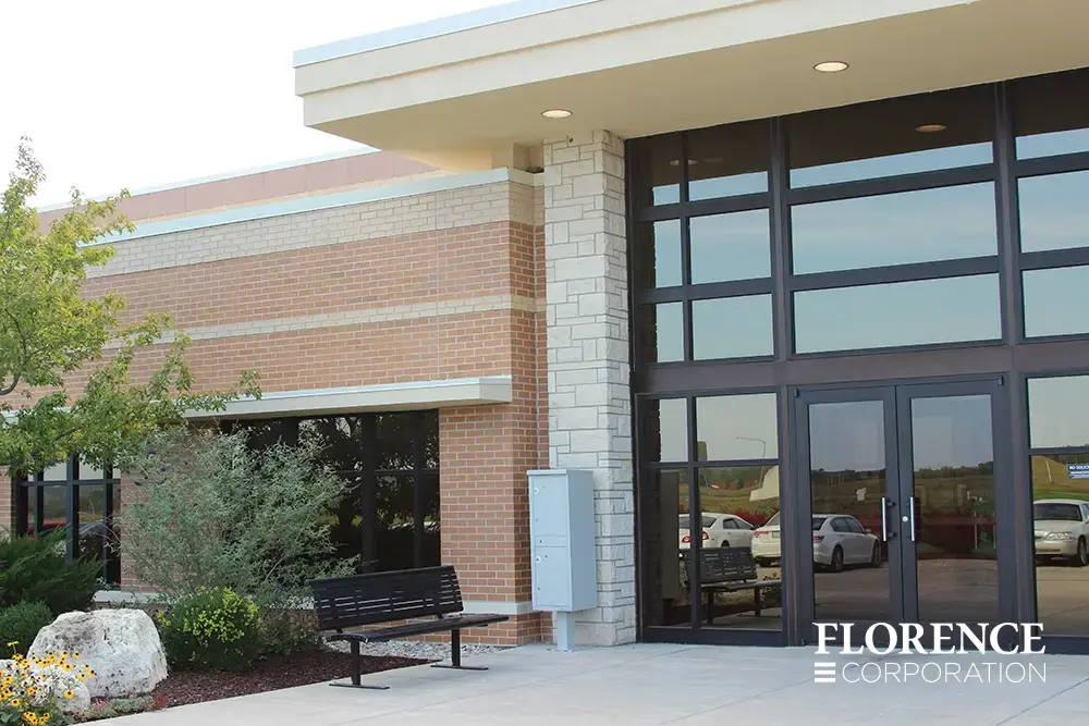 valiant&trade; outdoor parcel locker in postal grey installed in front of brick commercial building front door near bench and landscaping