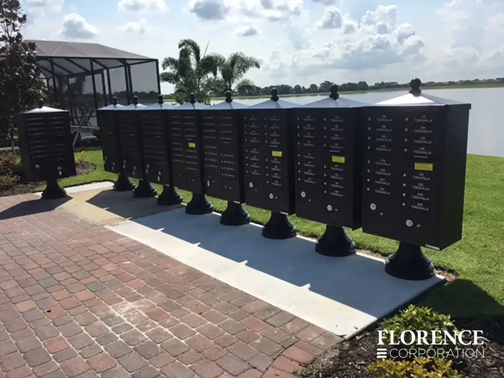 vogue&trade; accessories on vital&trade; cluster box units all in black installed on concrete slab on paver patio area in front of grassy lawn and a lake