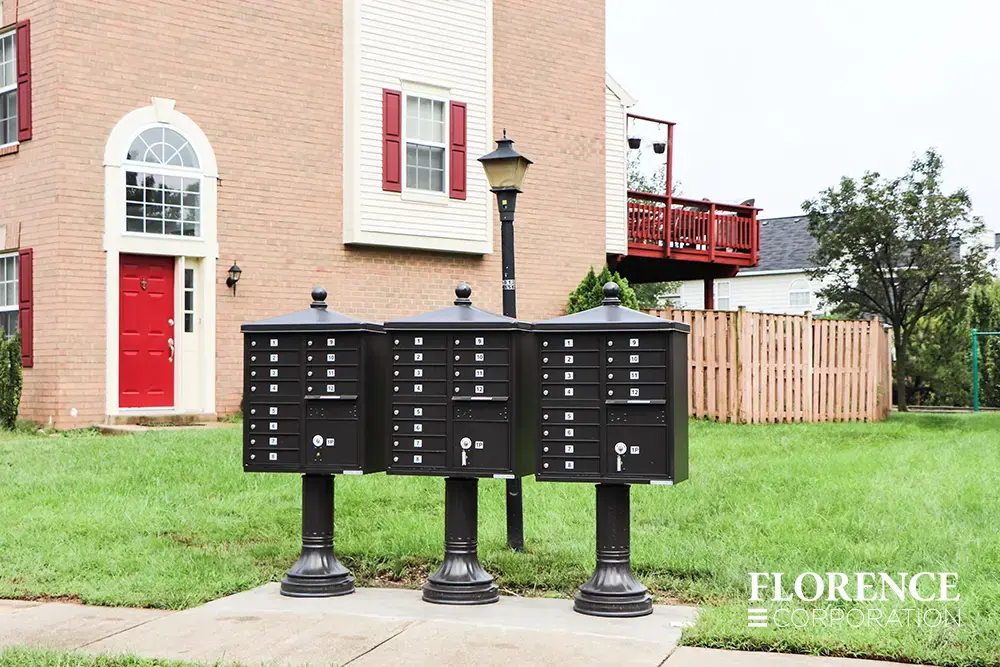 vogue&trade; accessories on vital&trade; cluster box units in black installed on concrete slab along side walk in multifamily townhome community with red brick building and red door