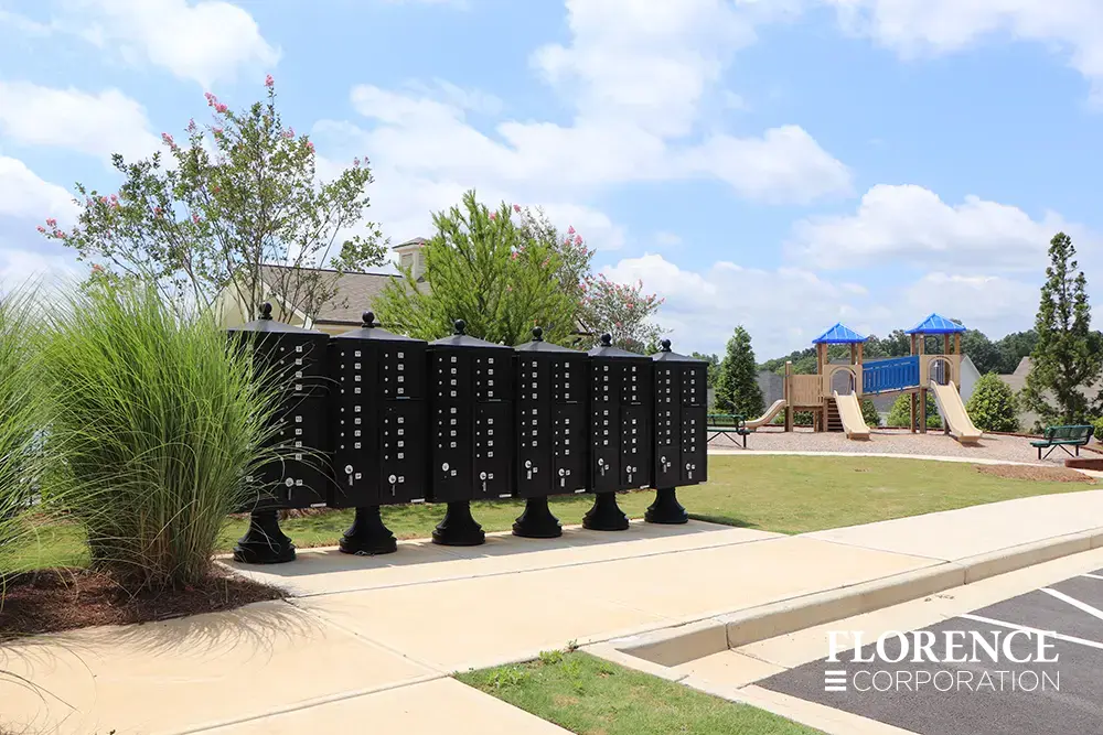 vogue&trade; accessories on vital&trade; cluster box units in black installed along concrete side walk near playground and community rec center