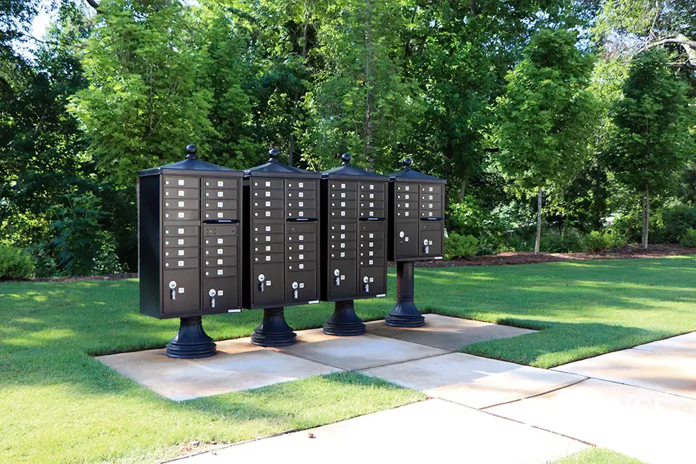 vogue&trade; accessories on vital&trade; cluster box units in black installed on concrete slab near grassy area with landscaping and trees