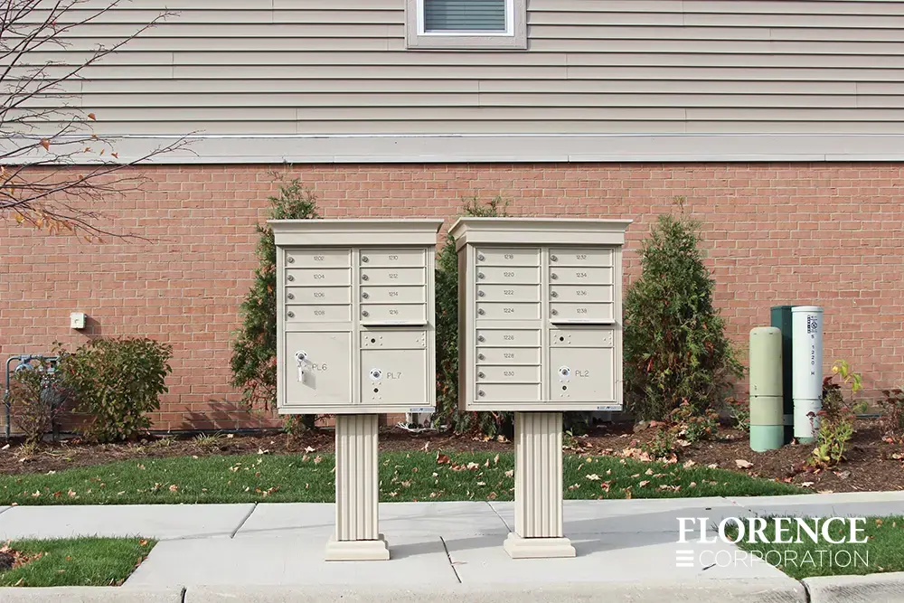 vogue&trade; accessories on vital&trade; cluster box units in sandstone installed in townhome community in front of red brick wall during fall with fallen leaves