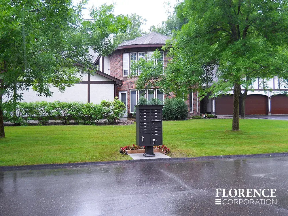 vogue&trade; accessories on vital&trade; cluster box units in dark bronze installed in single family community on grassy lawn on rainy day