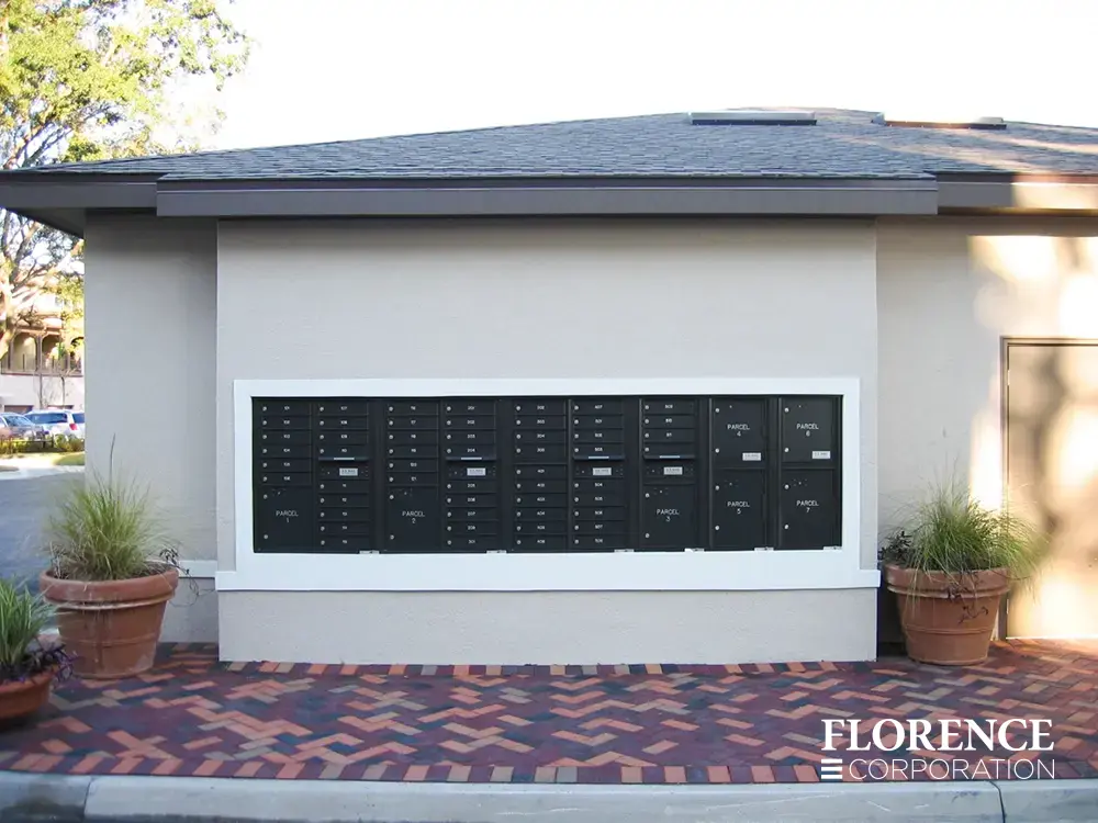 recessed mounted versatile&trade; 4C mailboxes and parcel lockers in black installed outdoors in wall with herringbone patterned pavers and green plants