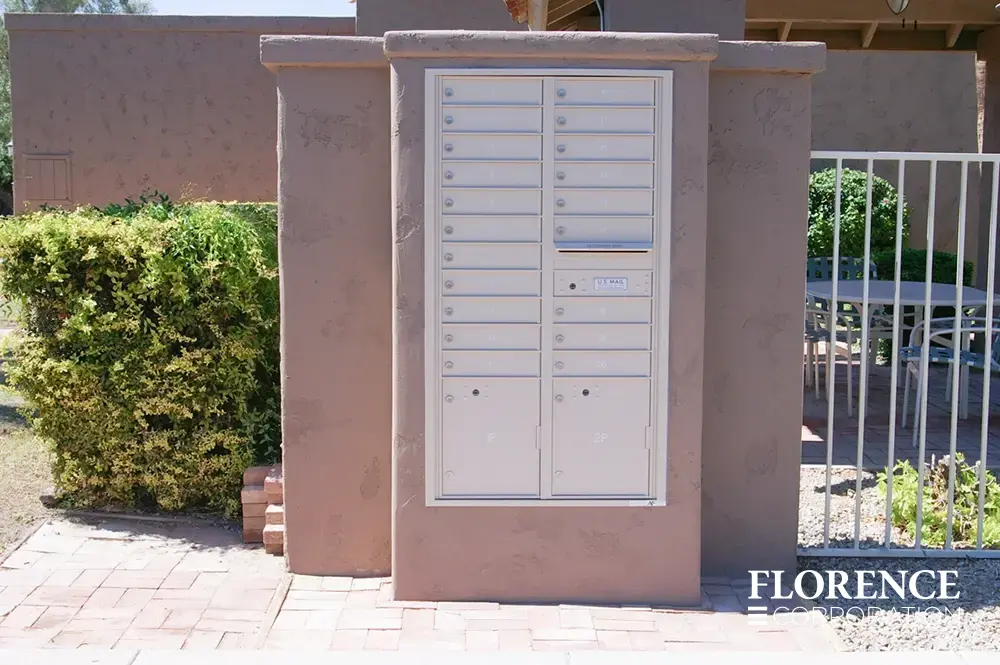 silver speck recessed mounted versatile&trade; 4C mailboxes in pick stucco wall near white fencing and green bushes