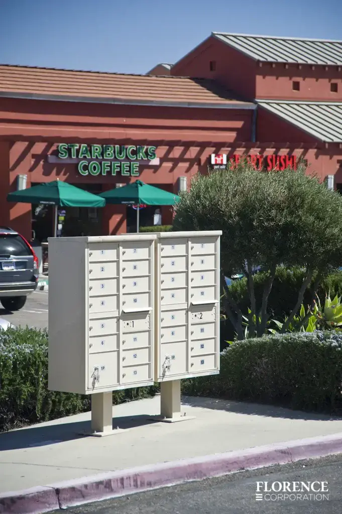 a pair of vital&trade; cluster box units in sandstone installed curbside outdoors in commercial strip mall near starbucks coffee and sport sushi parking lot
