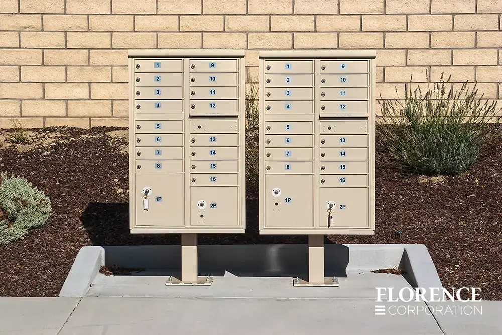 two vital&trade; cluster box units in sandstone installed side by side near shrubbery garden along sidewalk in residential community