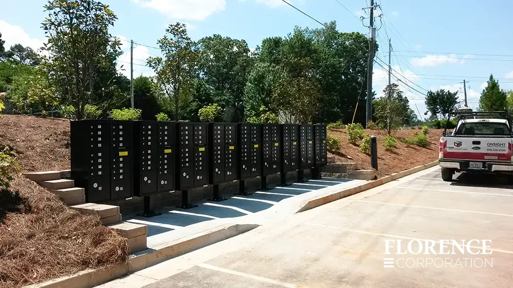 multiple florence vital&trade; cluster box units in black installed on concrete pad near parking lot surrounded by trees and landscape with truck parked nearby