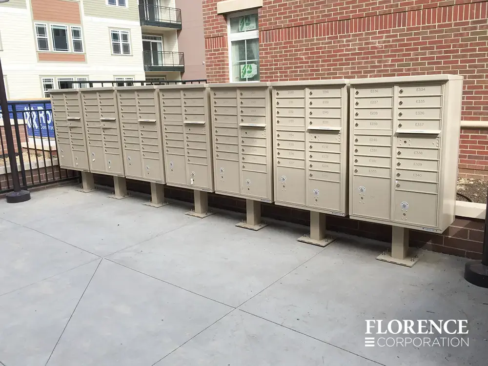 vital&trade; cluster box units in sandstone installed in a row along a brick wall in urban setting near multifamily apartment building