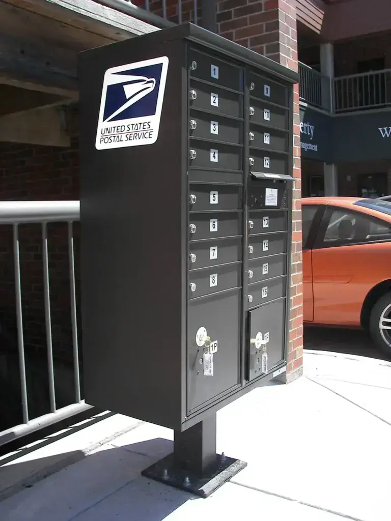 vital&trade; cluster box units in dark bronze with usps postal service logo on the side installed in commercial setting near parked orange car