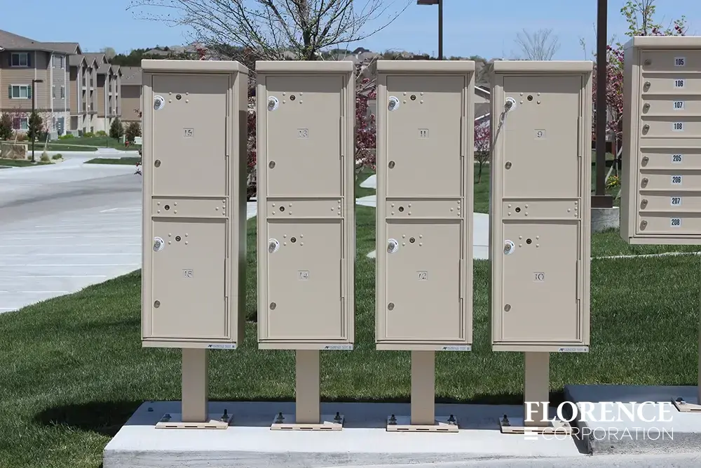 valiant-1590-OPL-series_008 multiple valiant™ outdoor parcel lockers in sandstone installed on concrete slab near cbu mailboxes, grass and parking lot of multifamily home community