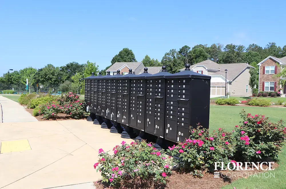 vogue-CBU-Accessories_024 vogue™ accessories on vital™ cluster box units in black installed in a line near pink floral landscaping with single family homes in the background.