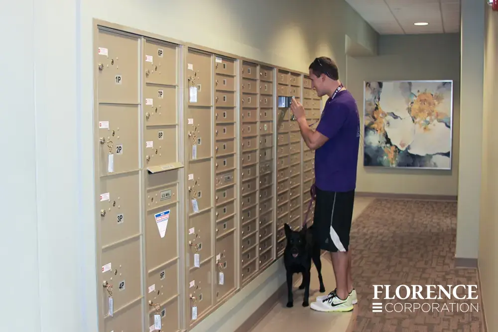 versatile-4C-indoor-install_006 Recessed mount versatile™ 4C mailboxes and parcel lockers in sandstone with man retrieving his mail holding a leash for a black dog