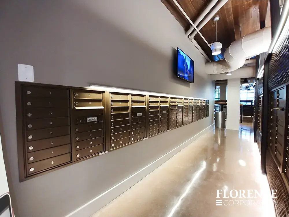 versatile-4C-indoor-install_033 Recessed mount versatile™ 4C mailboxes in antique bronze installed in mailroom lobby area of multifamily apartment building with wooden ceiling and mounted tv