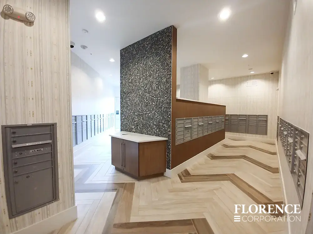 versatile-4C-indoor-install_035 Recessed mount versatile™ 4C mailboxes in silver speck installed in large expansive residential mailroom in multifamily building with herringbone patterned tile floor and wall paper walls