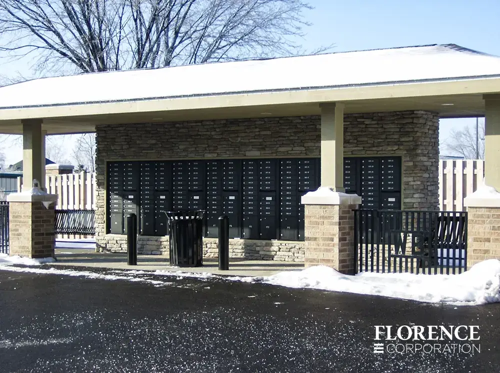 versatile-4C-recessed-indoor-40 row of black recessed mounted versatile™ 4C mailboxes in stone wall under covered pavilion with black trash bins, stanchions and railing