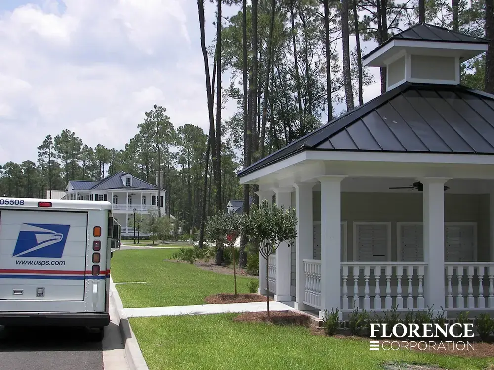 versatile-4C-recessed-indoor-48 recessed mounted versatile™ 4C mailboxes in silver speck installed under covered gazebo structure near grassy area with usps delivery truck parked in the street nearby