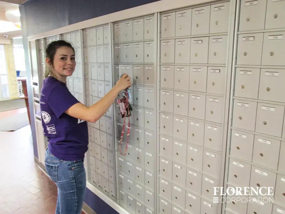 1700 Series 4B+ horizontal mailboxes in anodized aluminum installed in university dorm hall lobby with student in purple tee shirt checking her mail and smiling