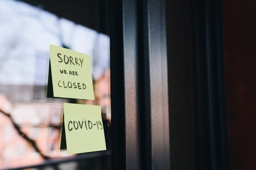 A window has two yellow sticky notes stuck to it. One says, Sorry, we are closed, and the other says, COVID-19.