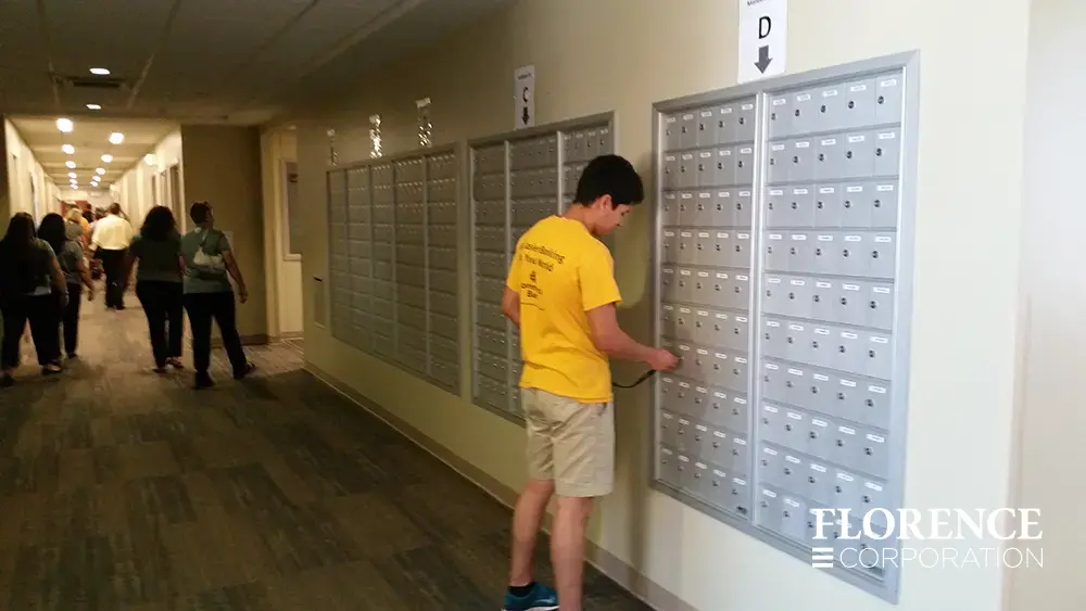 1700 Series 4B+ horizontal mailboxes in anodized aluminum installed recessed mounted in wall of busy university student housing dorm hallway with student in yellow shirt checking his mail